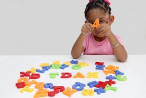 4 year old Latina brunette girl plays with colored letters and forms the word TDAH which means attention deficit hyperactivity disorder in spanish